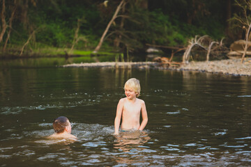 Two brothers swimming in river with strong current. Smiling while splashing in water.