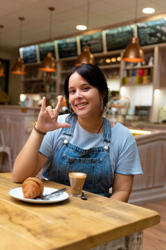 Young woman drinking coffee, making the sign of I love you
