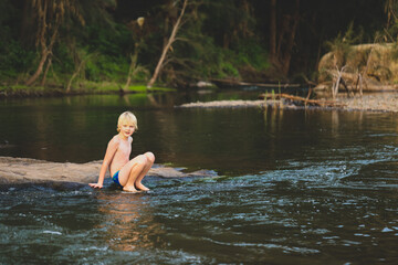 Boy sitting on rock looking at camera while swimming in natural swimming hole in central New South Wales, Australia