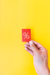 Percentage on a red background. Hand with a red postcard on a yellow background. Discount concept. Vertical photo.