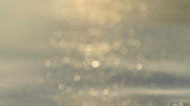 Soft sunlight reflecting on calm water surface with beautiful golden bokeh in the foreground, creating a peaceful dreamy atmosphere perfect for relaxation, wellness inspiration, and natural light aest