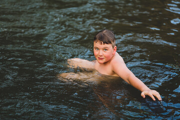 Boy swimming in river at dusk with big smile. Moody image with rich tones