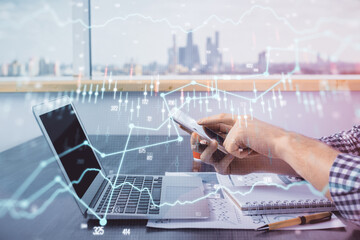 Double exposure of man's hands holding and using a digital device and forex graph drawing. Financial market concept.