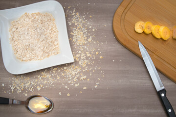 Desayuno saludable con ingredientes naturales que te brindan la energía necesaria para iniciar el día, banano, miel y avena en tabla de madera sobre mesón de cocina