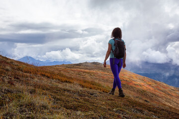 Fototapeta premium Adventurous Girl Hiking up the Nares Mountain during a cloudy and sunny evening. Taken at Carcross, near Whitehorse, Yukon, Canada.