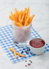 French fries potato chips in glass with tomato ketchup and pepper on blue restaurant paper.
