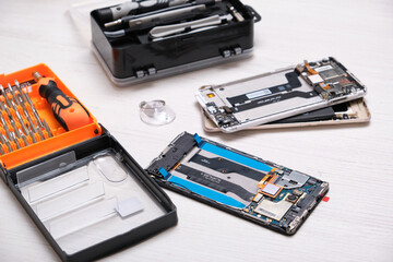 mini set of bits for a screwdriver in an orange box, a set for repairing a telephone and a broken smartphone on a wooden table, top view copy space