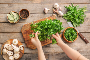 Woman with fresh parsley on wooden table, top view