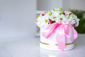 Bunch of flowers in a premium gift box with a pink ribbon, on a marble countertop.