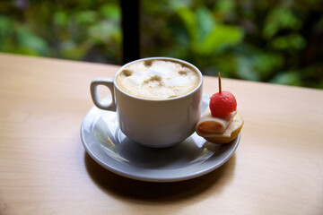 A Cup of hot coffee standing on the table. Cappuccino with cream, with canapes for appetizers.