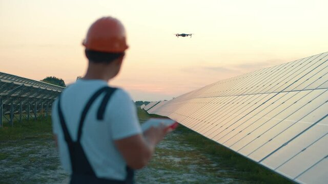 Workman using remote control to operate flying drone monitoring solar array software system. Solar panels producing clean energy. Renewable resources.