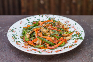 Close-up of vegetable wok with chicken. Selective focus on a healthy food with red and green bell peppers, carrots, soy sauce and seeds. Blur rustic background.