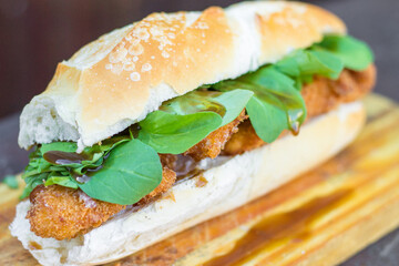 Tasty fried chicken and arugula sandwich with sweet and sour sauce on wooden board. Selective focus with blur rustic background.
