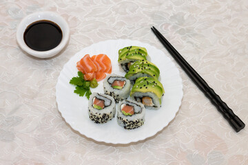Top view of japanese sushi plate. Salmon and shrimp rolls with avocado on white plate with decoration. Soy sauce and chopsticks on a table.