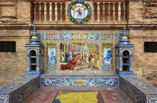 Image with the name of the spanish city of  Leon with a historical scene painted on ceramic tiles, with and the emblem shield above - seating benches in Spain Square in Seville