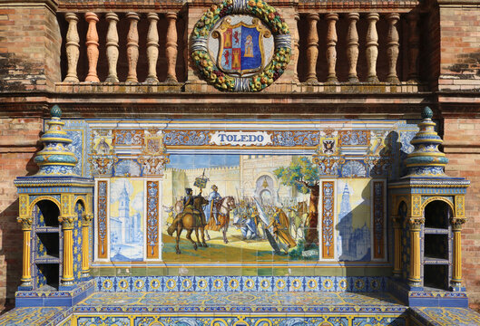 Image with the name of the spanish city of Toledo with a historical scene painted on ceramic tiles, with and the emblem shield above - seating benches in Spain Square in Seville