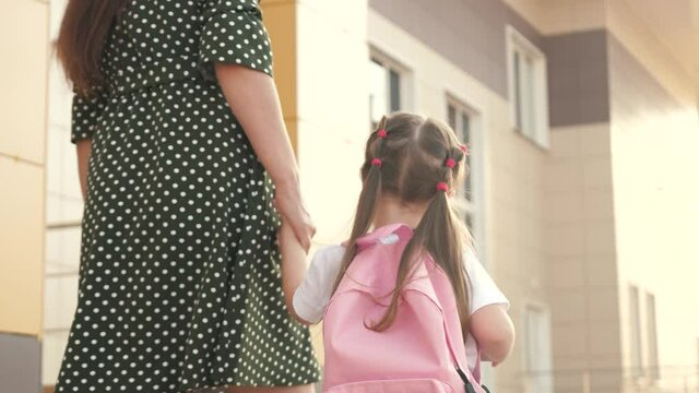 little daughter schoolgirl walks with backpack and holds her mother's hand. preschool education concept. happy family mother and child go to school holding hands.