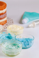 Fototapeta na wymiar White an blue icing in bowls with round sponge cake.
