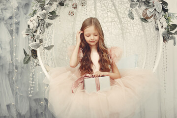 Cute little girl in a pink dress. Child sitting by the christmas gifts