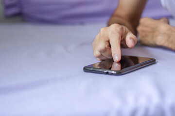 Man using a black smartphone on purple bed