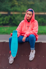 Young girl with short multicolored hair sits with skateboard in skatepark