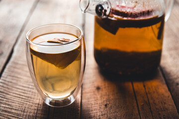 Citrus tea in a transparent teapot and a glass, healthy drink on a wooden background.