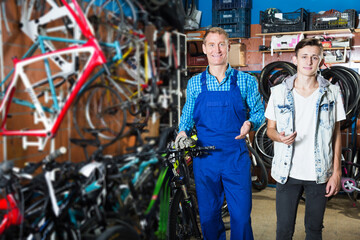 Man seller helping teenager boy to buy right bike in sport shop