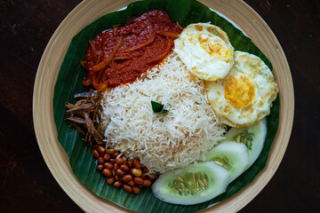 Traditonal Malaysia Asian food Nasi Lemak on a banana leaf in a wooden bamboo plate. Top view.