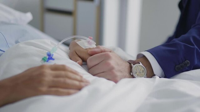 Caucasian man holding hand of sick woman in hospital bed