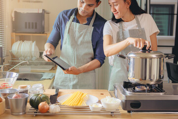 Happiness Asian couple using smart pad while cooking in kitchen together at home