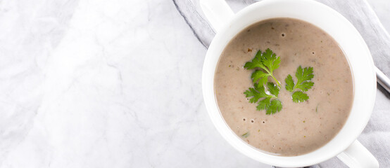Champignon mushroom cream soup in white bowl on marble table. Top view, copy space, banner image