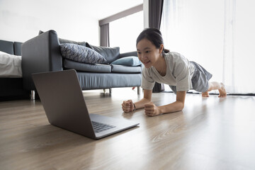 Healthy asian child girl is doing plank exercise and push up,strong fitness girl watch live workout online on laptop computer,vigorous physical exercise or training at home,healthy lifestyle concept.