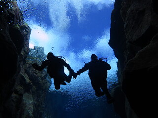 Silhouette of couple swimming in Silfra, Iceland, glacial water taken from 20m looking up at clouds