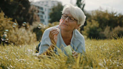 Retired senior woman enjoying freedom. Childish grandma blowing soap bubbles in the park. High...