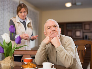 Frustrated aged man sitting separately at home while dissatisfied woman angrily rebuking him. Family conflicts concept