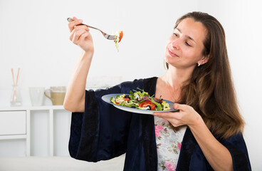 Young pretty woman eating vegetable salad from plato in bed at home