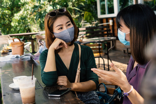 two Asian female customer wearing protective mask talking at the cafe and drinking coffee together, new normal and social distancing lifestyle concept