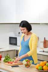 Pregnant Woman Mixing Fresh Green Salad On Kitchen.