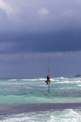 Distant traditional pole or stilt fishermen on a stormy day in Koggala, on the south west coast of Sri Lanka.
