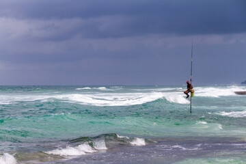 Distant traditional pole or stilt fishermen on a stormy day in Koggala, on the south west coast of Sri Lanka.