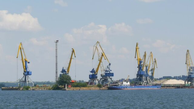 A row of construction or cargo cranes on the banks of a river or pond against the background of a barge standing nearby