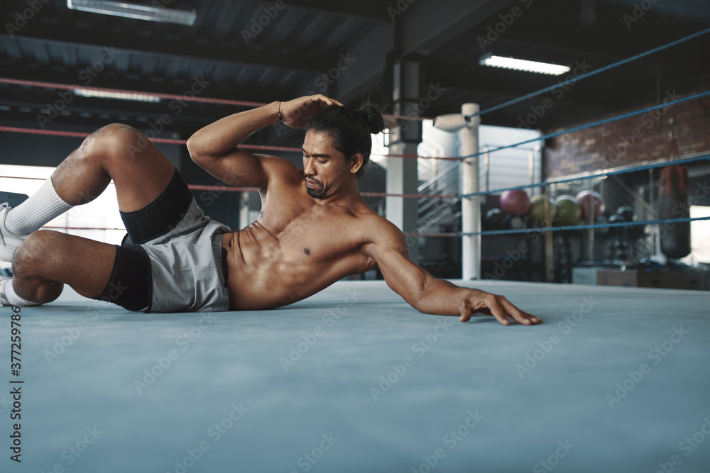 Wall mural Gym. Man Doing Abs Workout On Boxing Ring. Shirtless Asian Sportsman Exercising On Floor At Fitness Center. Portrait Of Topless Sexy Handsome Guy With Strong, Healthy, Muscular Body Warming Up Indoor.