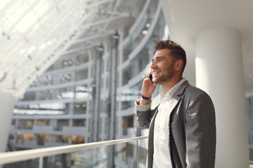 Handsome businessman in a suit and talking on the phone on the street. Portrait of a young man in business style smiling and laughing.