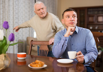 Fototapeta na wymiar Frowning adult man listening to reprimanding from his aged father at home..
