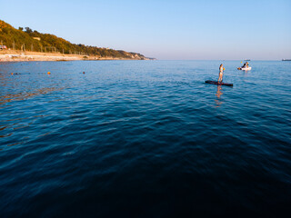 Obraz premium Attractive Woman on Stand Up Paddle Board, Woman paddling on sup board and enjoying turquoise transparent water. Tropical travel, wanderlust and water activity concept. Sunset and relax