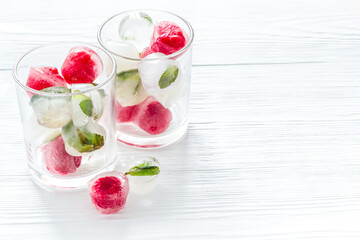 Cocktail glasses with berries in ice cubes on white table copy space