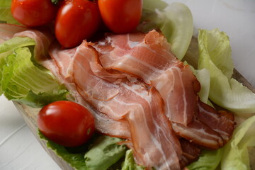 Raw bacon slices on lettuce leaves