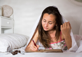 Smiling woman elaxing under blanket and making schedule for tomorrow in bedroom