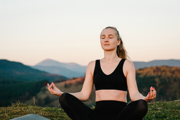 Fototapeta na wymiar Young girl doing yoga fitness exercise outdoor in beautiful landscape. Morning sunrise, Namaste Lotus pose. Meditation. A woman is practicing yoga at mountains. Relax in nature.