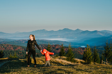 Fototapeta na wymiar Mother and daughter, enjoying time together, walking on sunset on top of foggy mountain. Tourists on background autumn nature. Hikers on sunlight in trip in country Europe. Happy family.